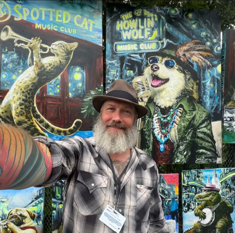 Ocean Clark wearing a brown fedora and a gray-and-white plaid flannel shirt takes a selfie in front of a colorful outdoor mural featuring illustrated cats and a sign that reads 'The Howlin' Wolf Music Club.'.